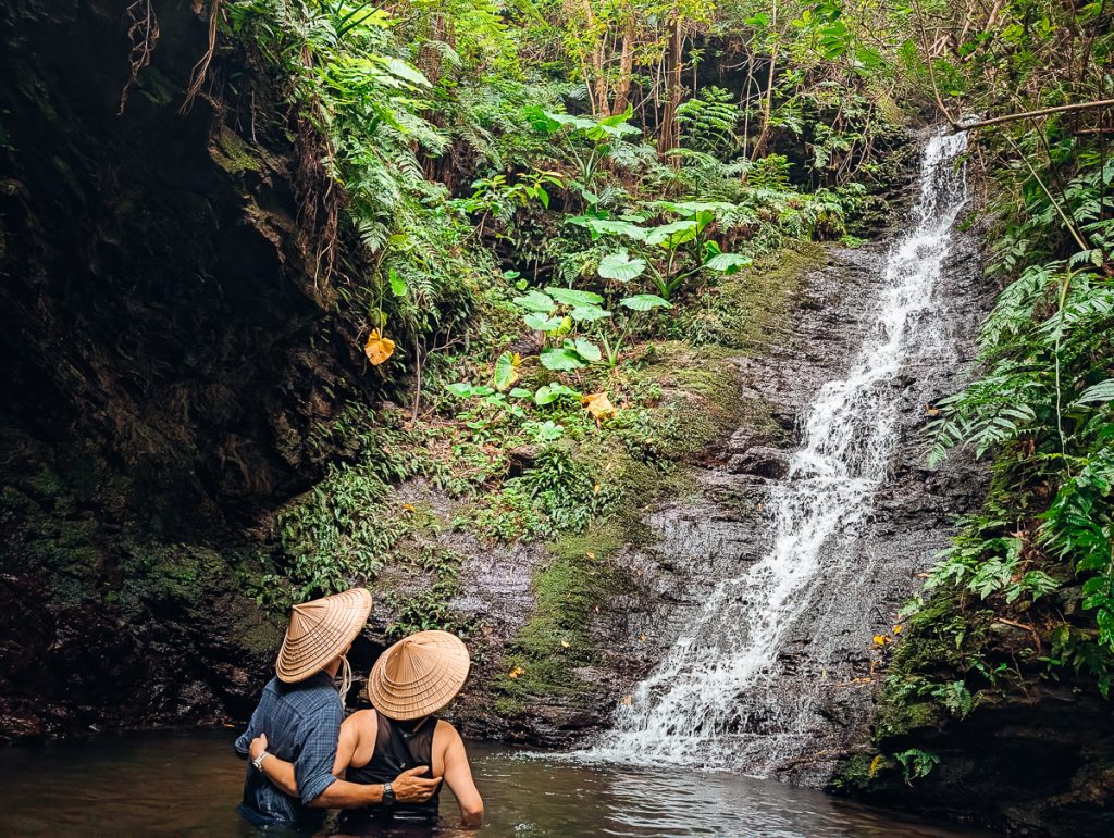 Two people with Okinawa hats look at a waterfall