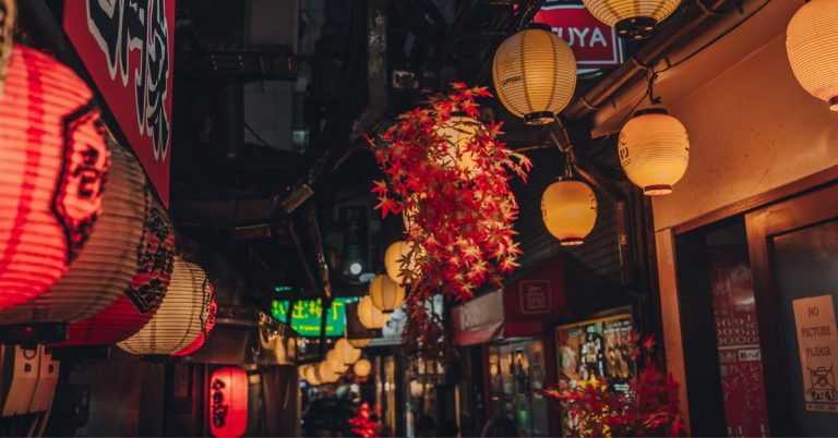 A night-time photo of a narrow street lined with lanterns, signs and lights.