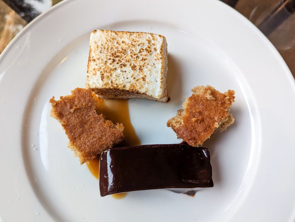 A very close up overhead shot of a white plate with four small pieces of food that look like a kind of deconstructed s'more.