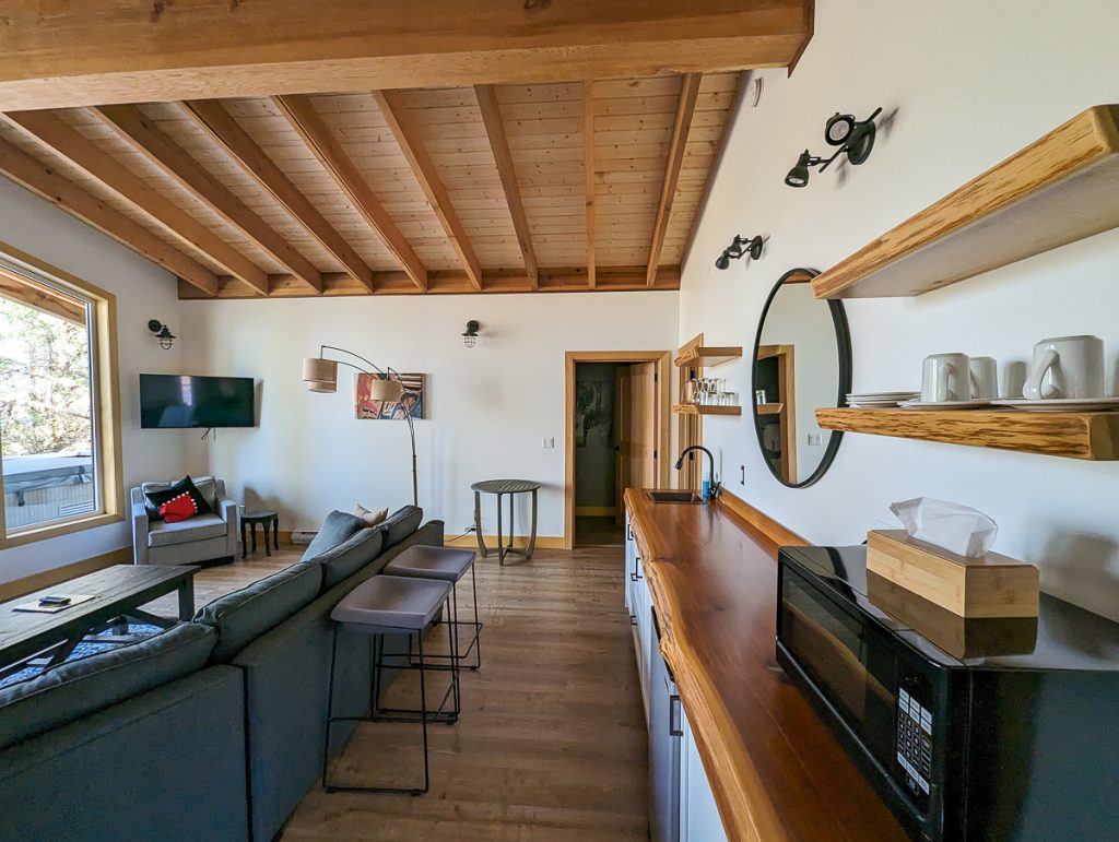 A living room and kitchen with a big couch and exposed wooden beams on the ceiling.