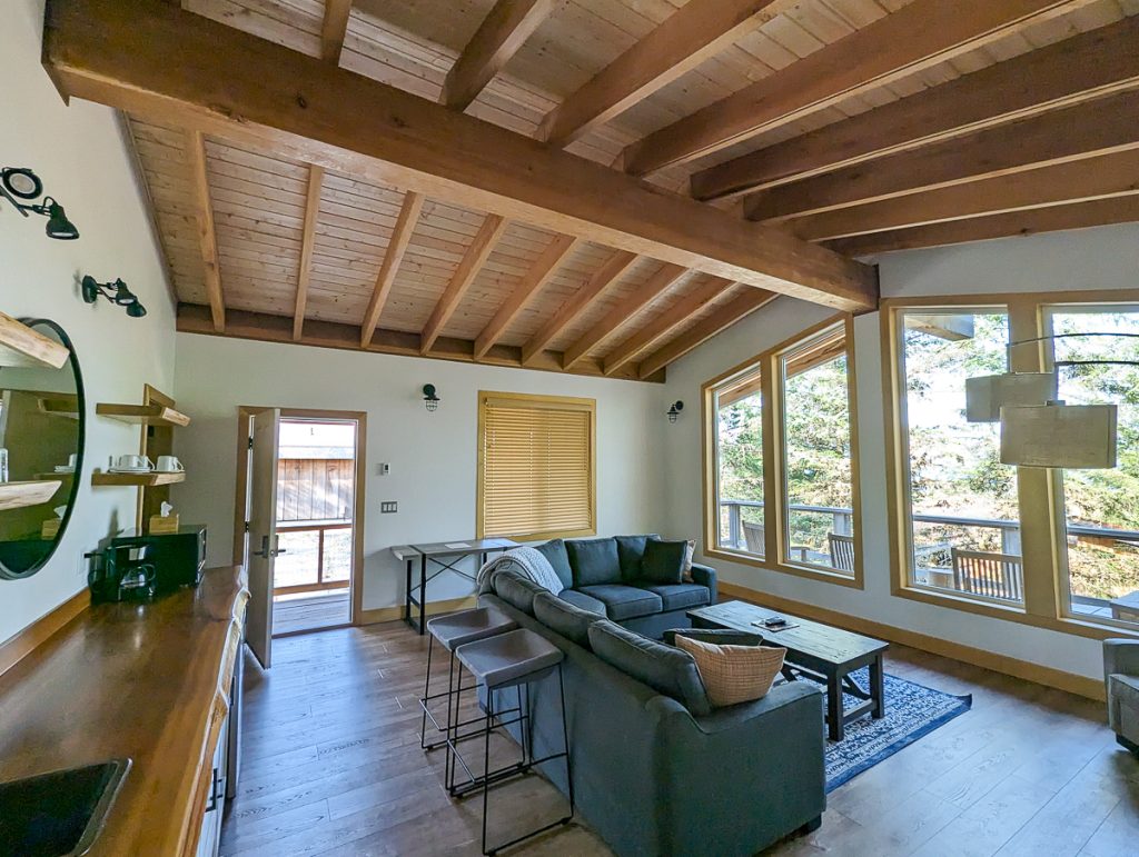 A room with white walls and exposed timber beams in the ceiling with a couch and small kitchenette.