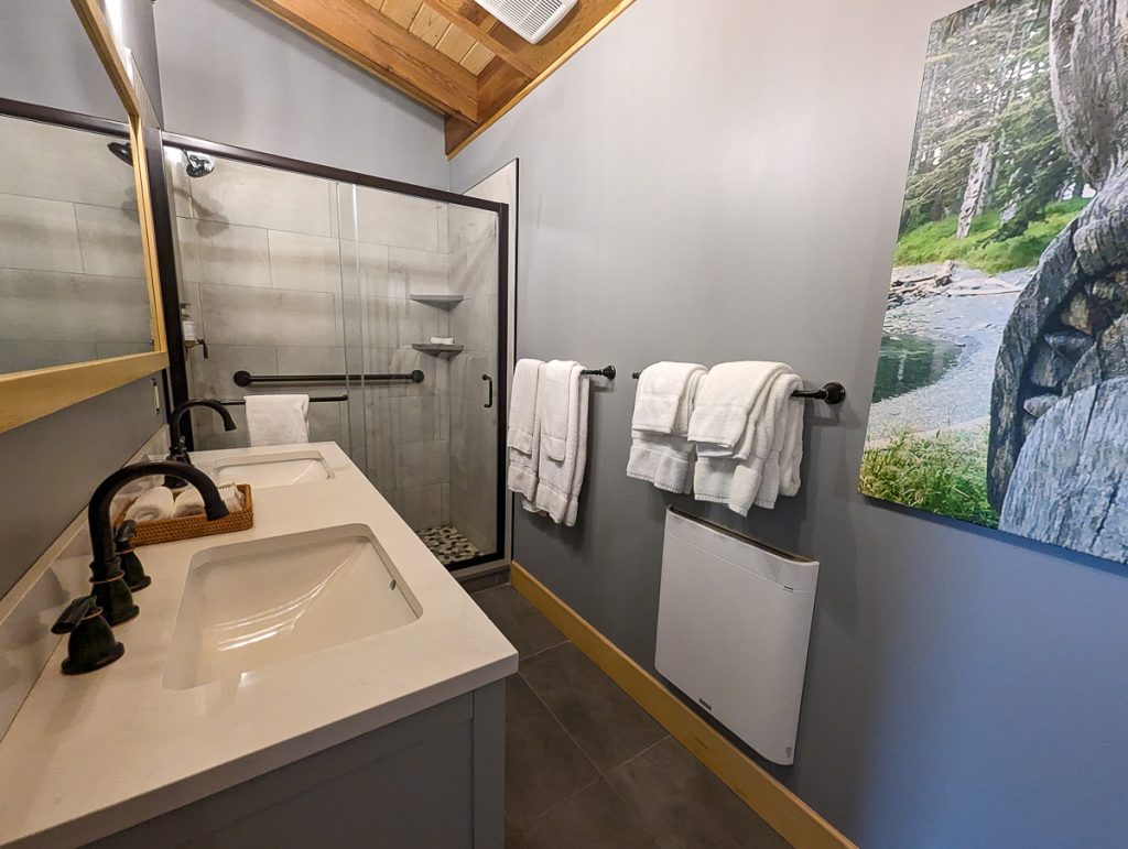 A hotel bathroom with a large stone-floored shower, white towels hanging on rails and a canvas showing a natural landscape on the wall.