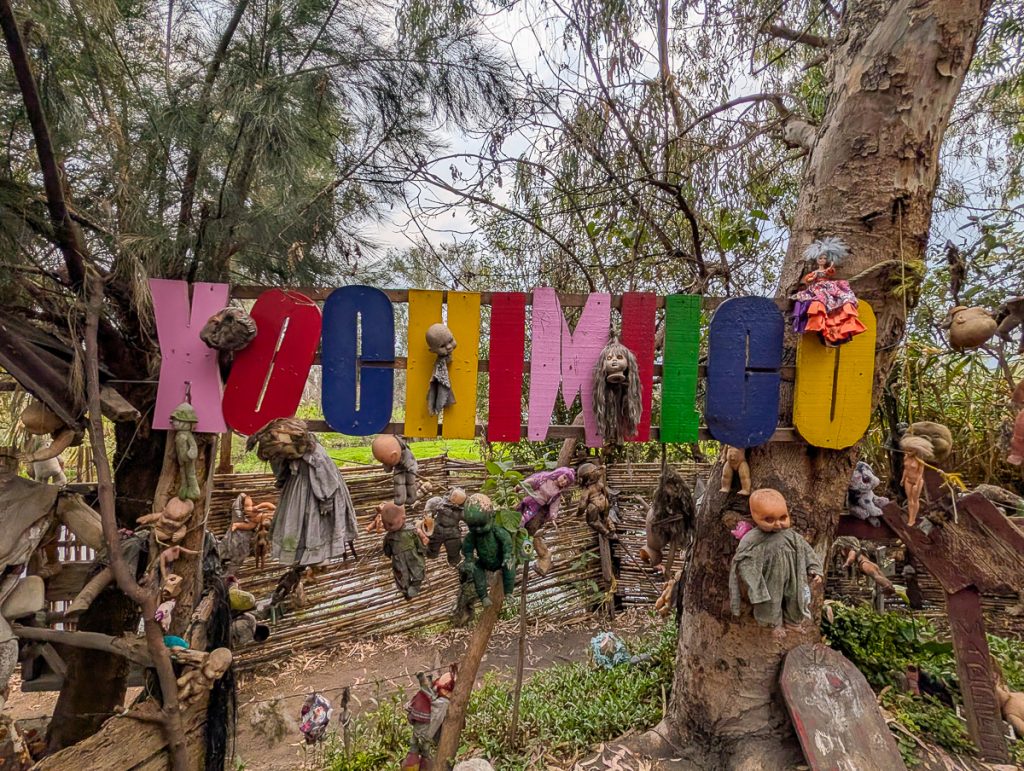 Lots of weathered dolls hanging off some trees and a colorful sign that says "Xochimilco."