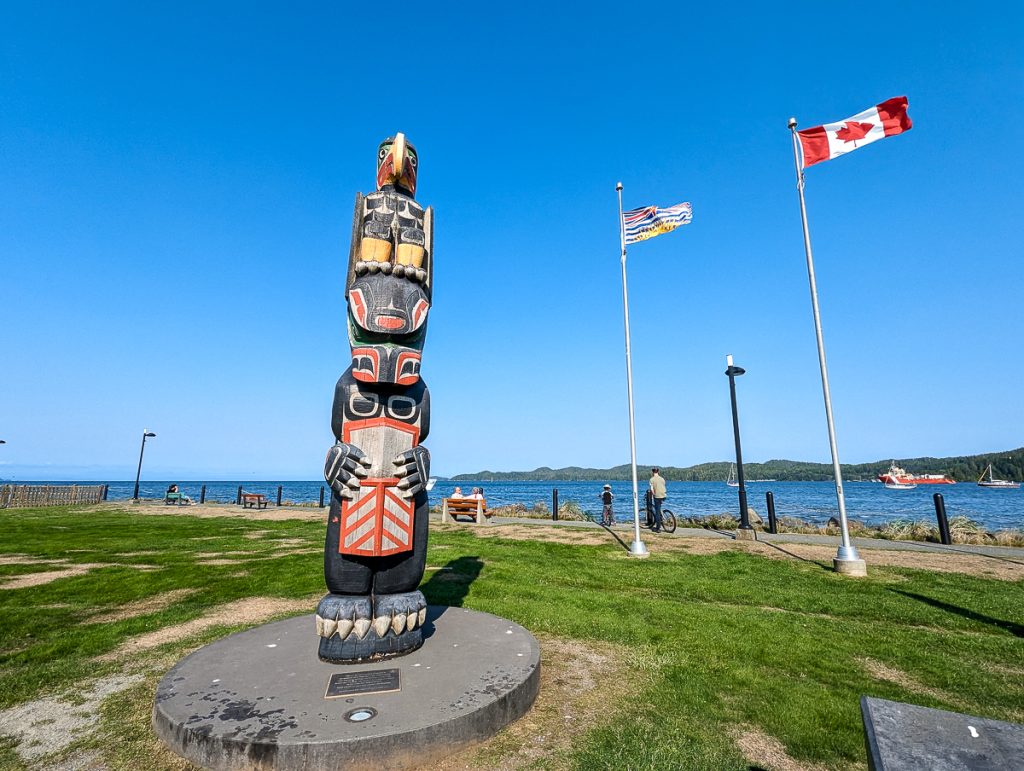 an Indigenous totem pole and the Canadian flag in a Port Hardy park