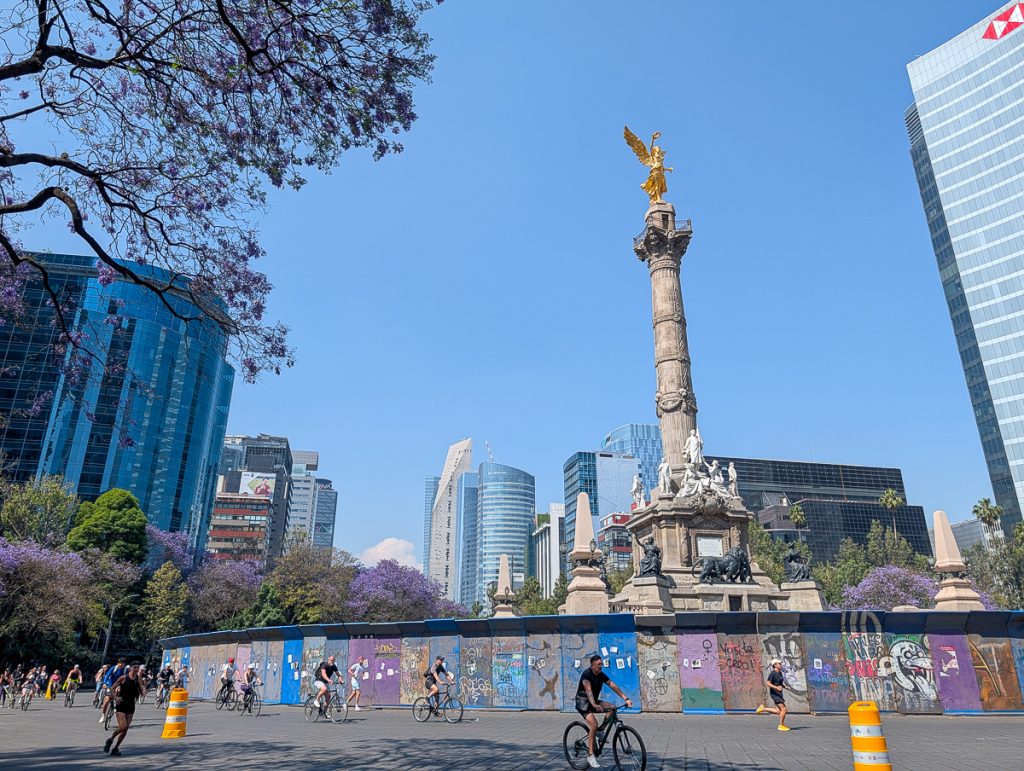 a group of people run and bike in Mexico City near a monument of an angel 