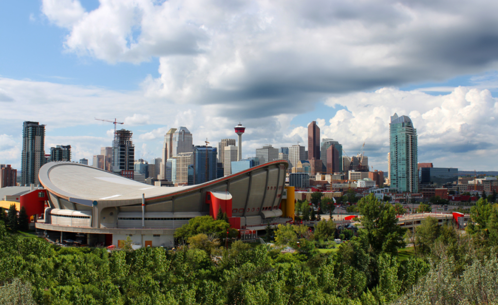 A view across trees and the Calgary Saddledome to skyscrapers and Calgary Tower under a cloudy sky,