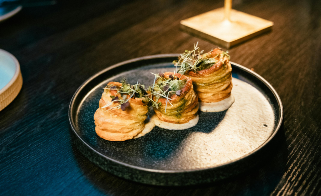 A close-up shot of a fancy black plate with three pastry towers topped with greenery.