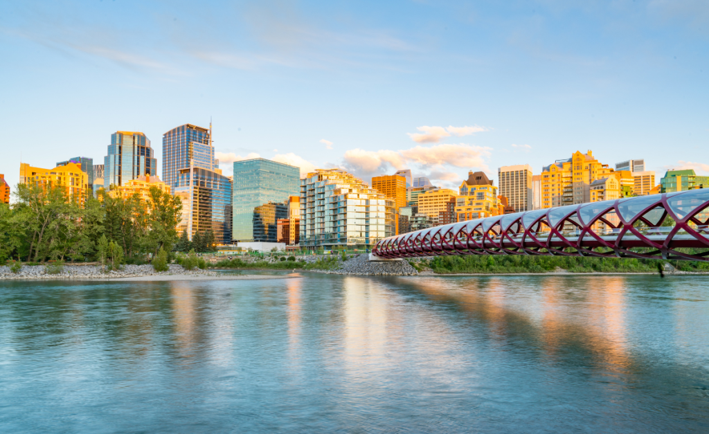 Calgary river around sunset, with the red Peace Bridge leading towards city buildings lit up in gold.