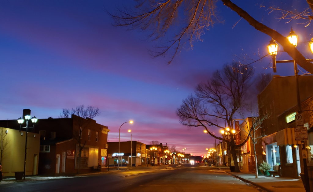 A wide city street lit up at dusk with no people around.