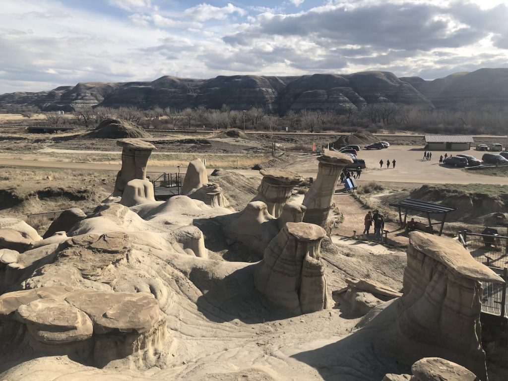 People walking from a car park along a path next to strange rock formations in an arid landscape.