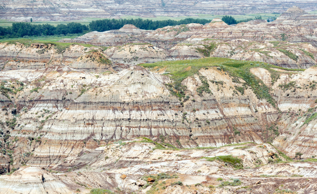 A view across hills with different colored layers of rock and green grass on top.