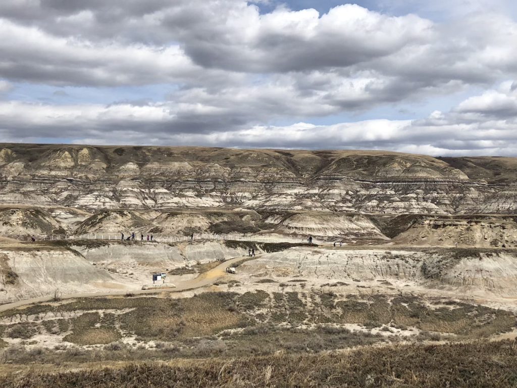 A series of rocky hills with walking paths and people in the distance under a cloudy sky.
