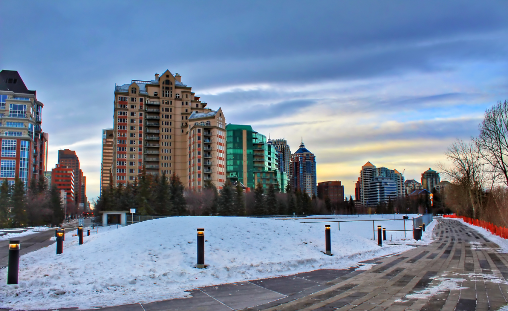 A park covered in snow with tall buildings behind and moody clouds above.