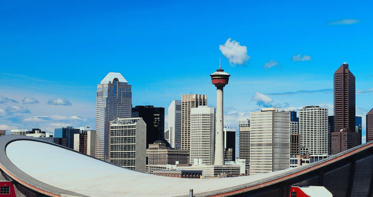 A view across the Saddledome arena in Calgary towards Calgary tower and skyscrapers with blue sky and fluffy white clouds behind.
