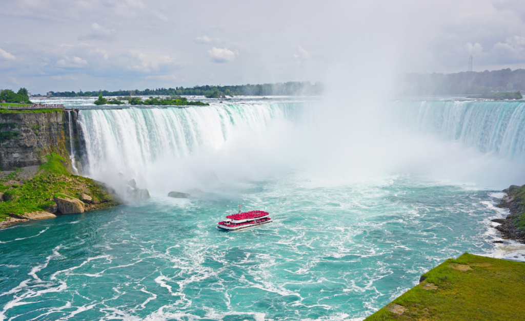 A boat filled with people in red raincoats at the base of Horseshoe Falls at Niagara Falls.
