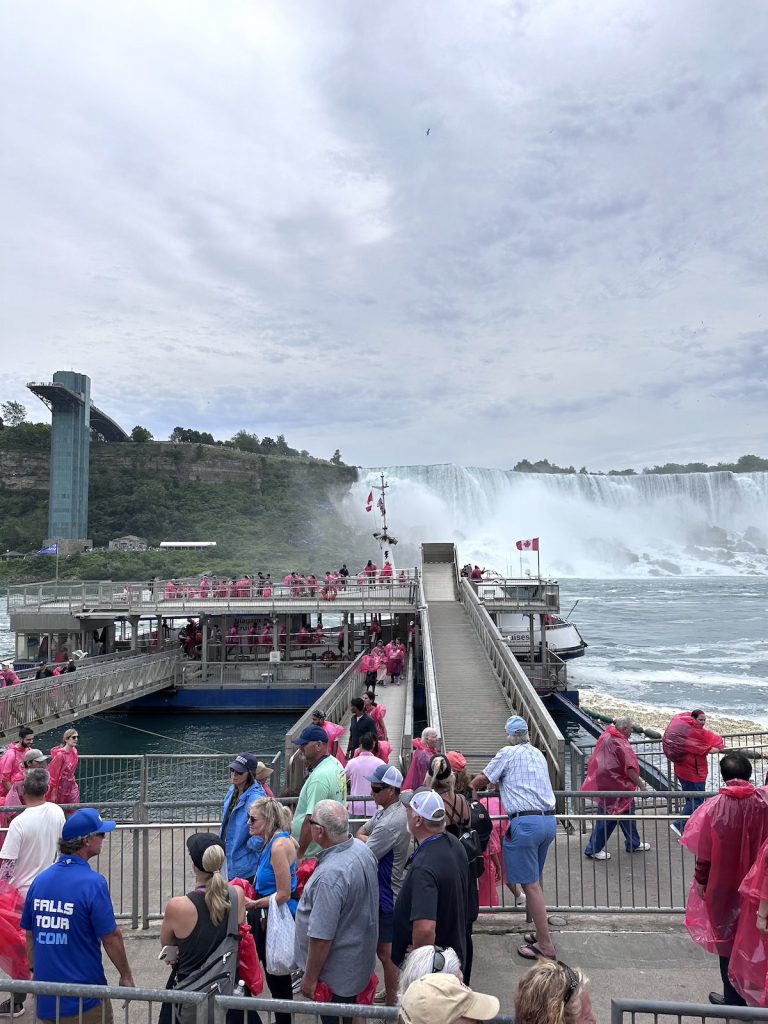 People lining up to get on a cruise boat at Niagara Falls on the Canadian side with the American Falls in the background.