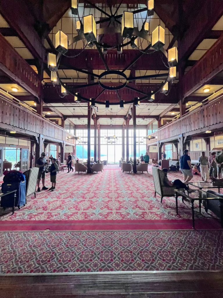 A spacious room with internal balconies, carpet and people sitting in chairs under a large chandelier.