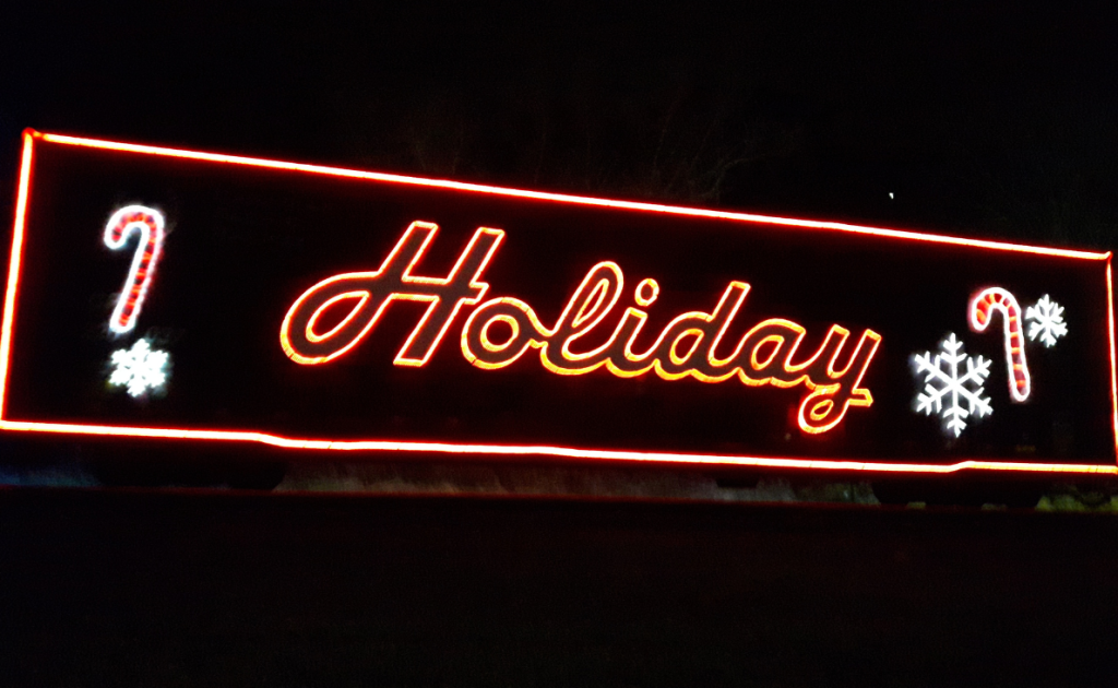 A sign lit up on a black background with a red border, red text that says "Holiday" with some candy cans and snowflakes.