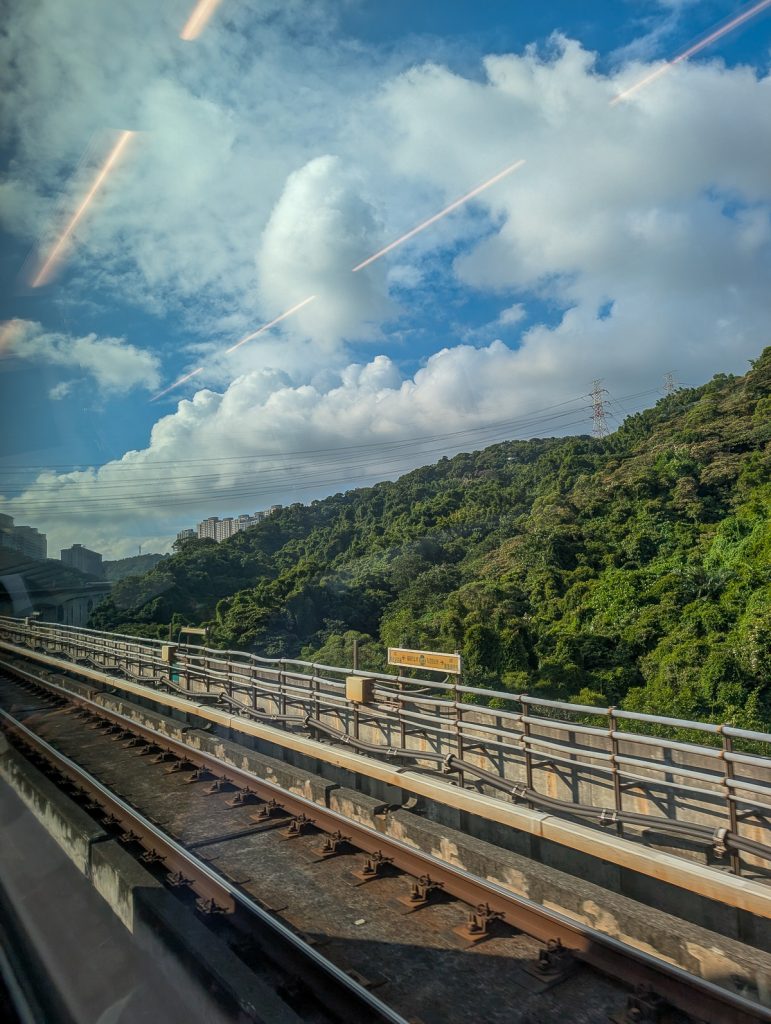 Lush greenery next to a train line with a city peeking from behind.