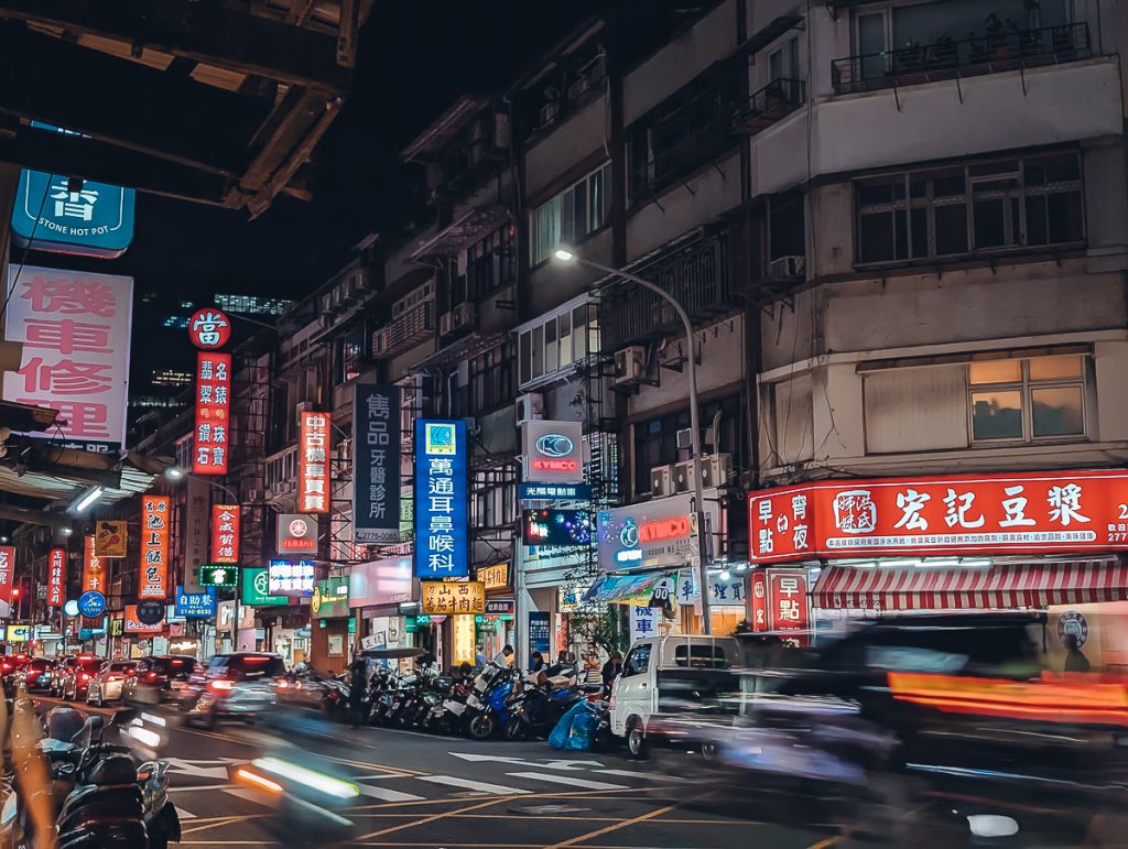 A Taipei street at night with lots of neon signs and traffic.
