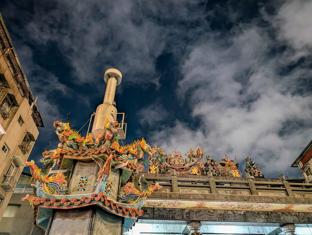 An ornate gate at night with colorful dragon statues on top.
