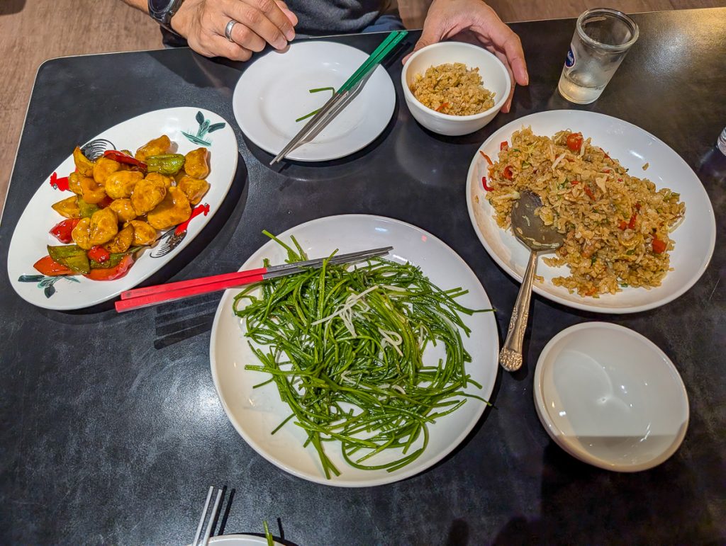 An overhead shot of plates of vegetarian Chinese food on a table with someone's hands just in shot.