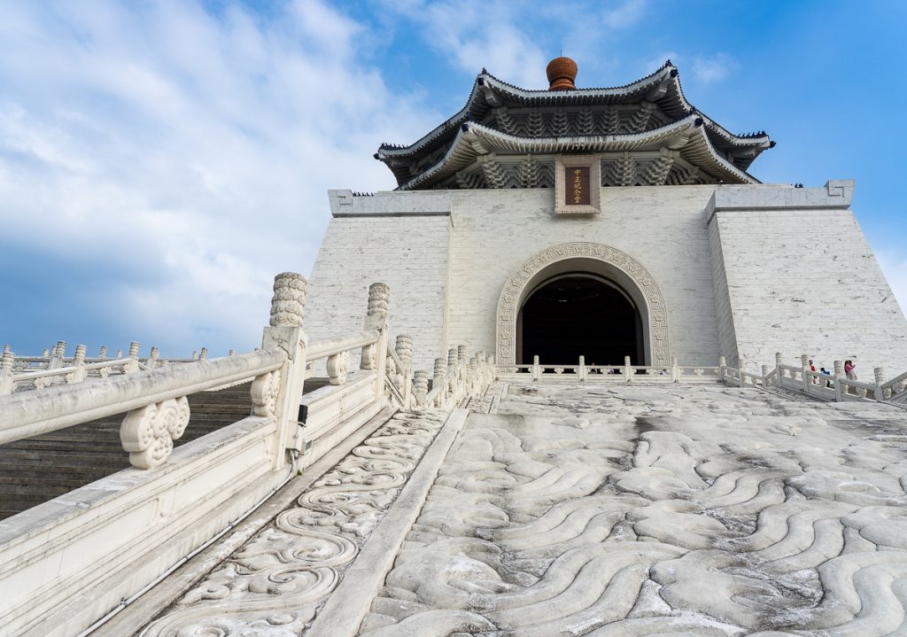 A grand white temple seen from below the white, marbled path to the arched doorway.