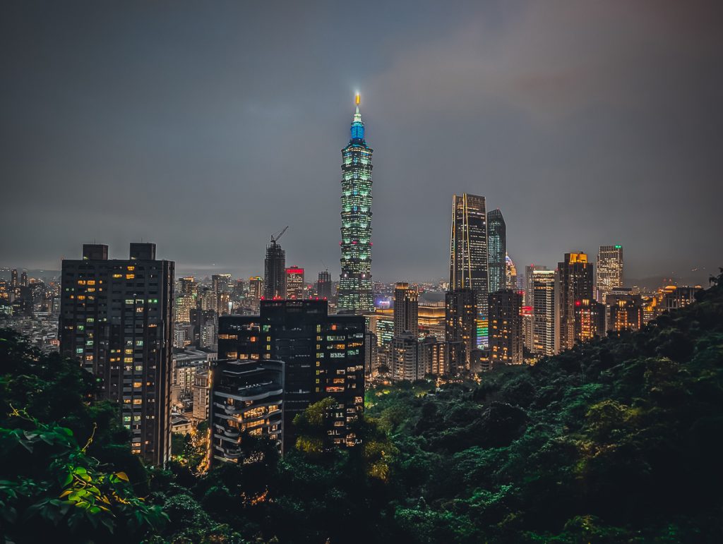 A view over Taipei at night from Elephant Mountain, with greenery in the foreground and all the skyscrapers lit up in the background.