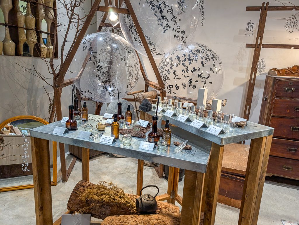 A fancy shop display of glass bottles on tables, with clear balloons covered in script above.