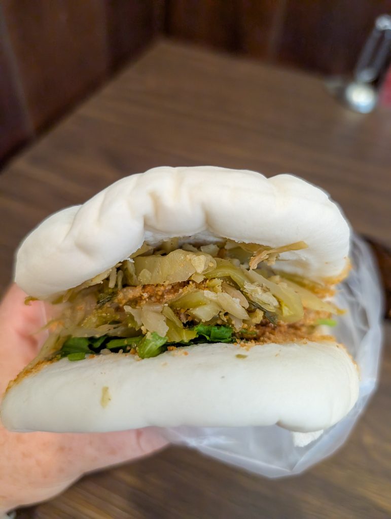 A close up of a hand holding a Gua Bao bun to show the green vegetable filling.