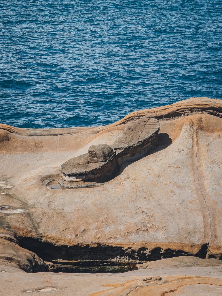A sandstone rock formation that looks like a sandal, next to water.