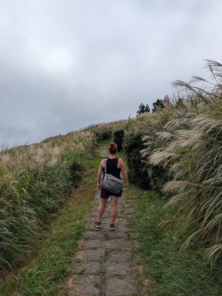 Sooz standing on a stepping stone path on a hill with her back to the camera and thick clouds ahead.