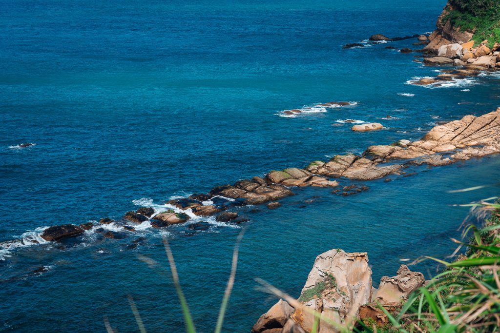 A photo taken from a hill looking down at square-shaped rocks in water.