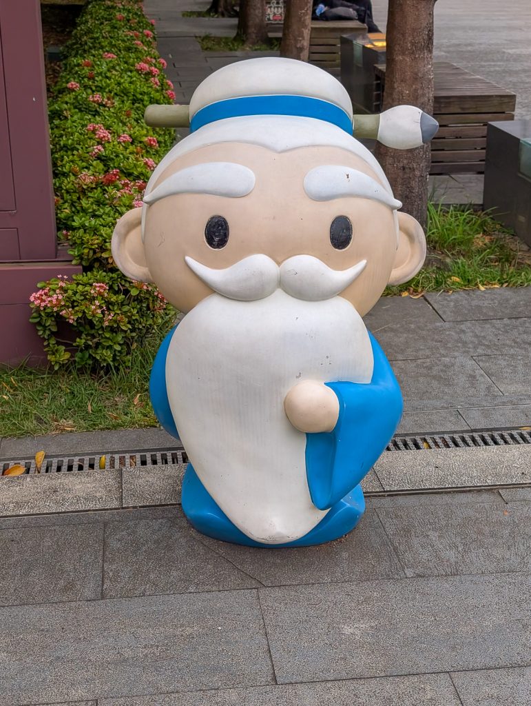 A cartoon-style statue of Confucius on a pathway.