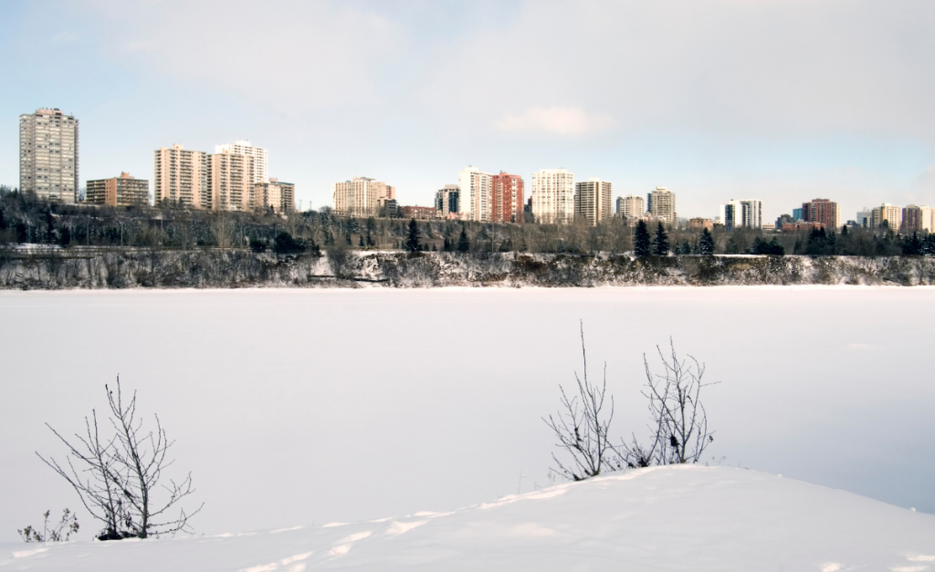 City buildings seen from behind an embankment across a smooth field of snow.