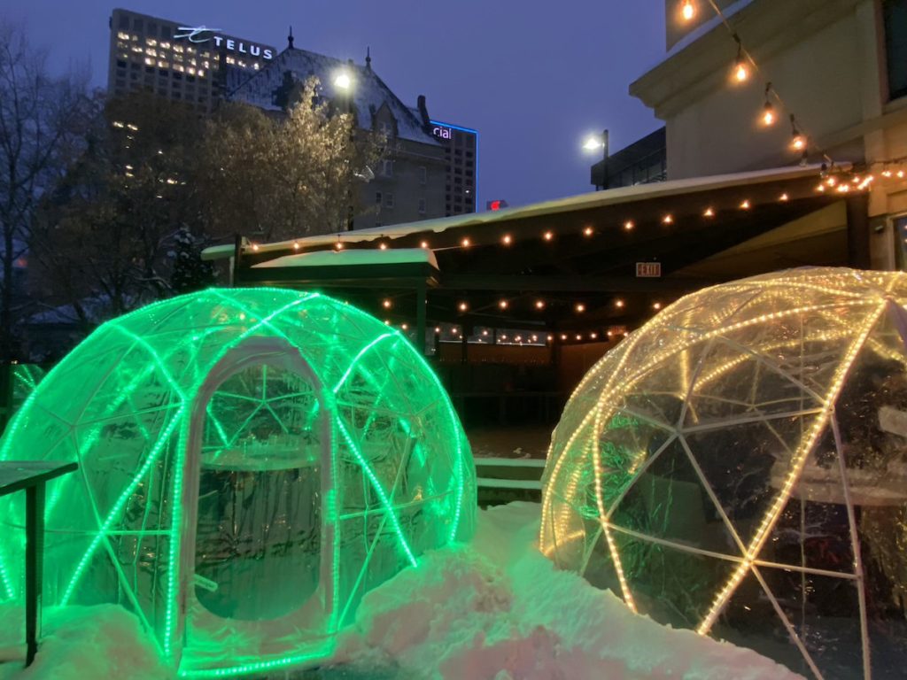 Two blow-up igloos lit up at night in a hotel courtyard surrounded by snow.