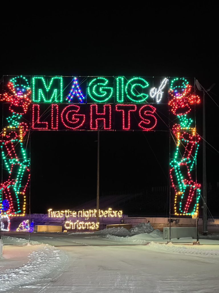 A sign at night lit up with Christmas symbols and the words "Magic of Lights."