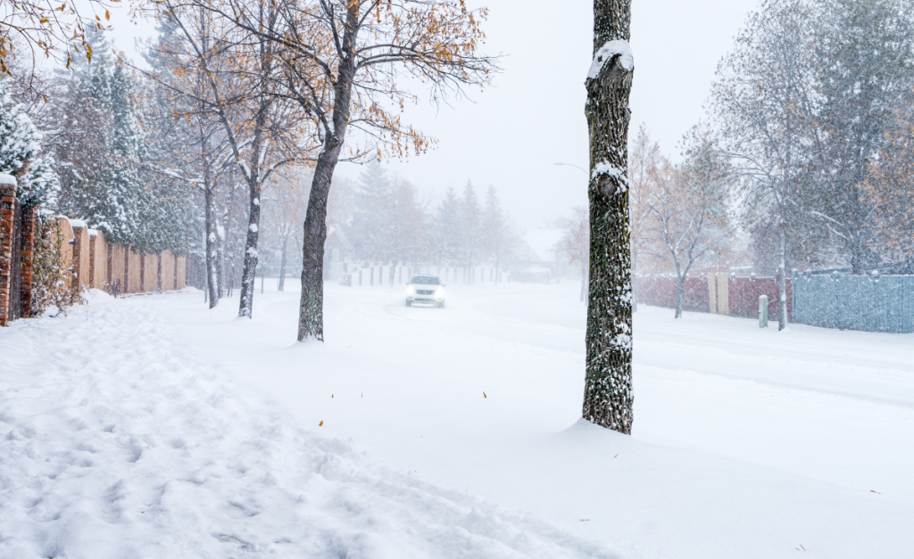 A car driving on a snowy road with snow still falling and piled up on the sides of the road.