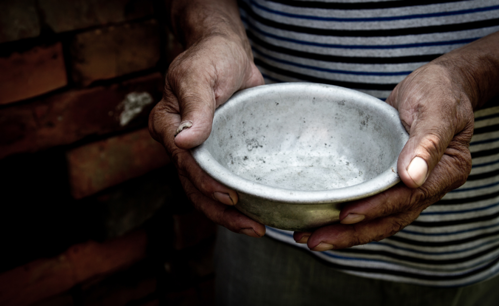 A close up of the dirty hands with chipped nails of a person in a white and black striped shirt holding an empty bowl in front of bricks.