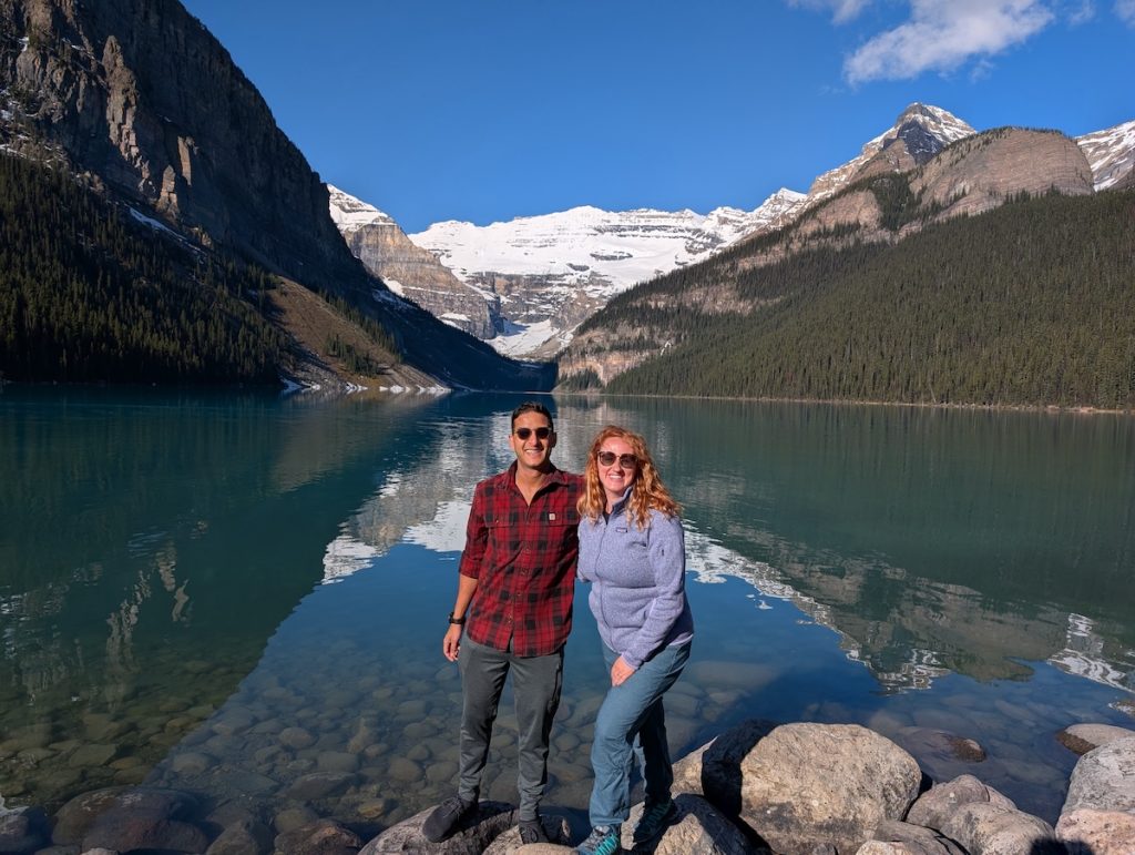 two people stand in front of Lake Louise with snowy mountains in the back