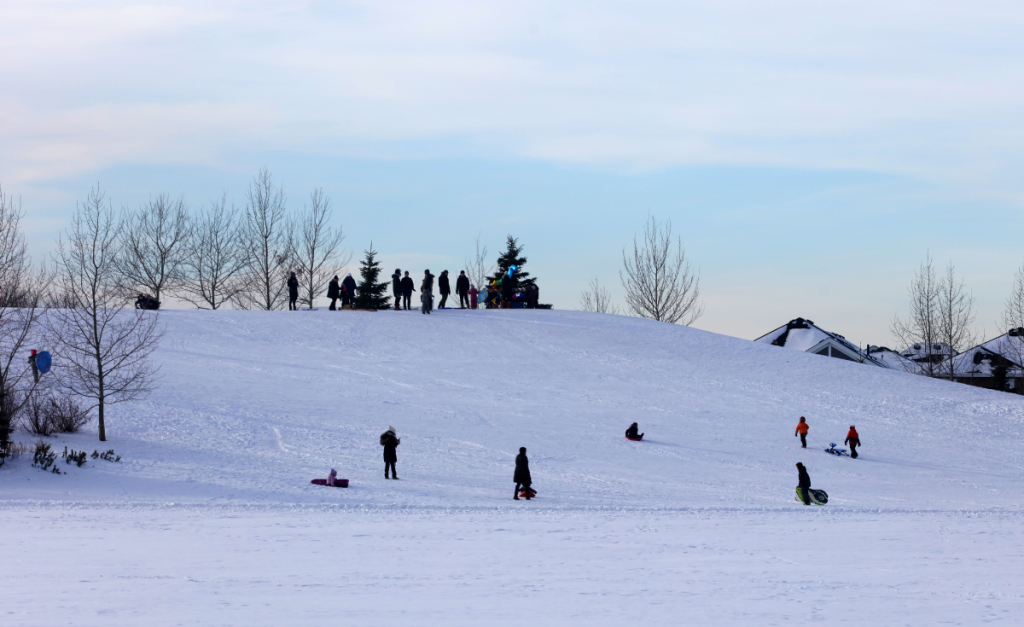 A small hill covered in snow with people standing or sledding on it.