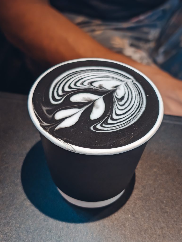 An extreme close up of a black and white drink with foam art in a black paper cup.