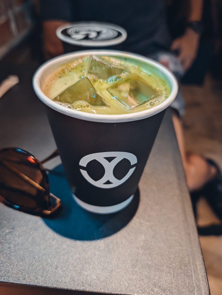 A close up of a green drink with ice  in a black paper cup.