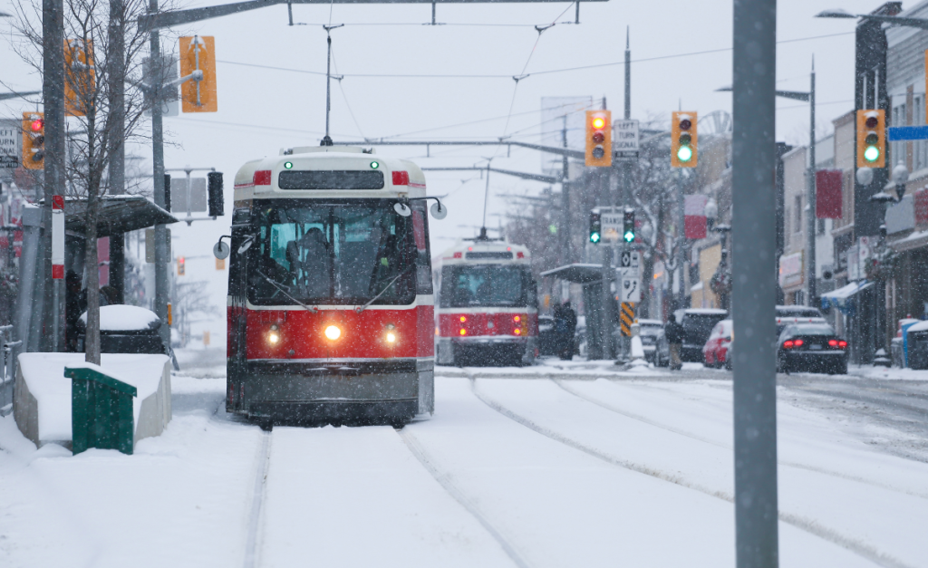 Trolleybuses and cars on a very snowy city street.