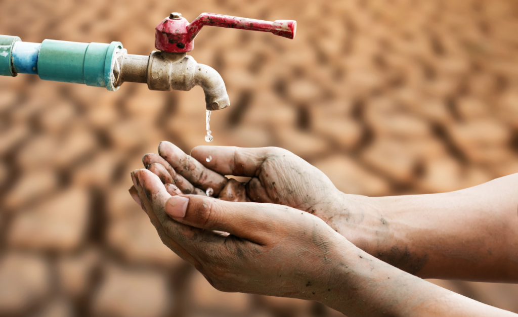 Two grubby hands cupped under a dripping faucet with dry dirt in the background.