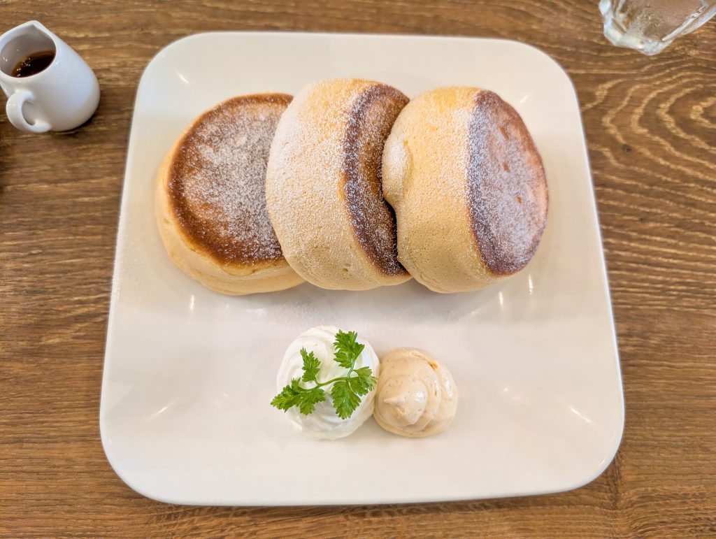 An overhead close up shot of a square white plate with three Japanese souffle-style pancakes.