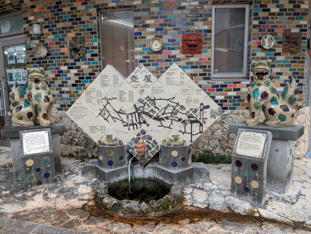 A street display of two lion dogs on plinths with a small pond in between and a large map of the area with everything written in Japanese.