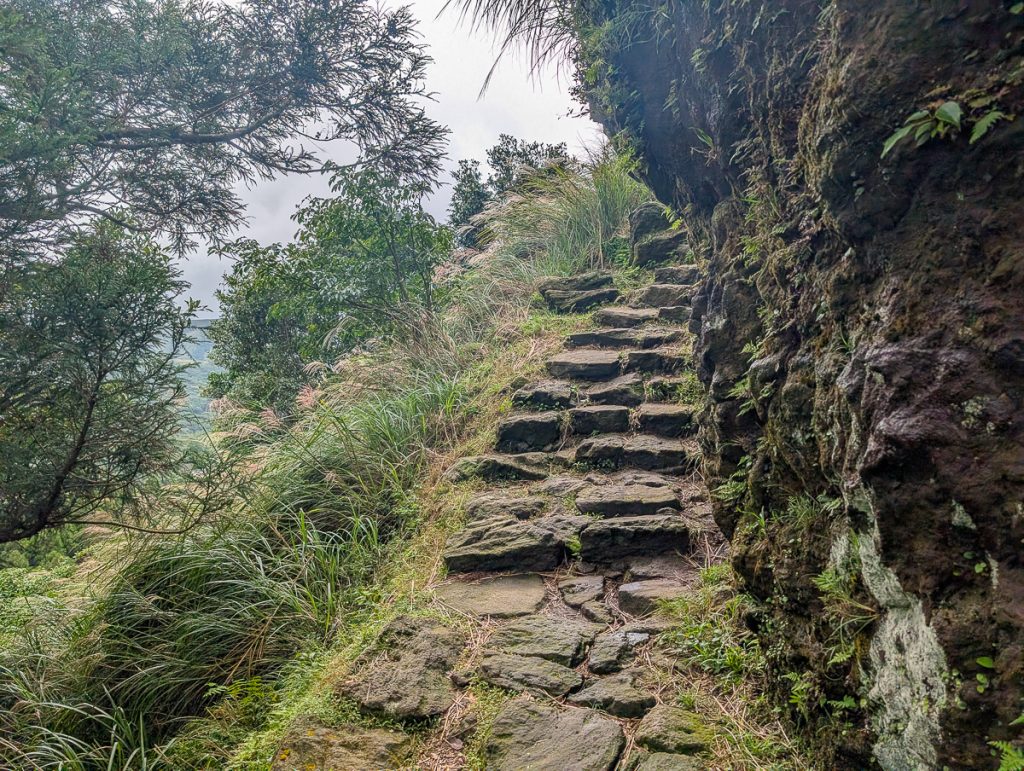 A path of stairs made of rocks on a steep hill next to a rockface.