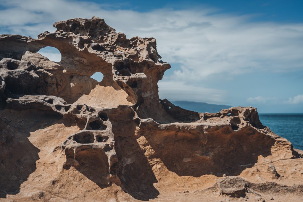 A close up of rock next to water with strange shapes and holes due to erosion.