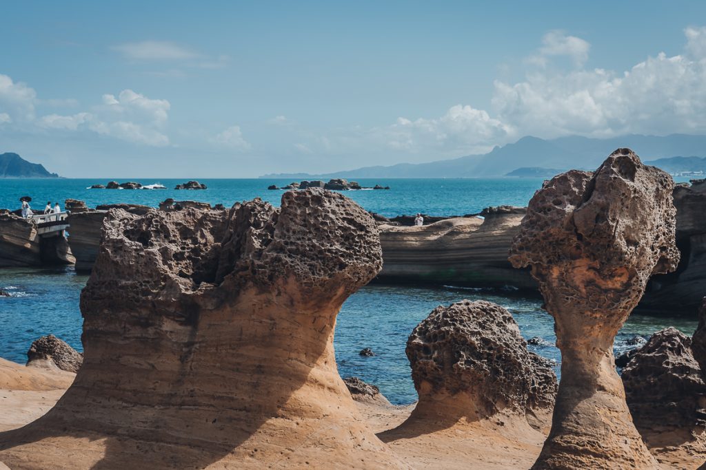 A group of sandstone rocks in strange shapes next to water on a sunny day.